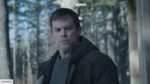 Michael C. Hall's Dexter wearing a black coat over a grey sweater, in a snowy wood, with the sun beaming behind him