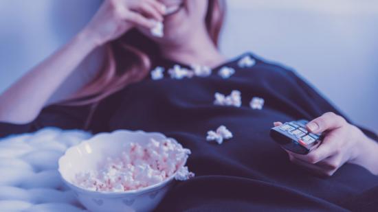 Best Amazon Prime VPN: image shows a woman smiling and eating popcorn while she watches television, safe in the knowledge that her VPN is on.