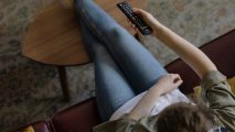 Best Hulu VPN: image shows a person on a sofa holding a TV remote from a top down view.