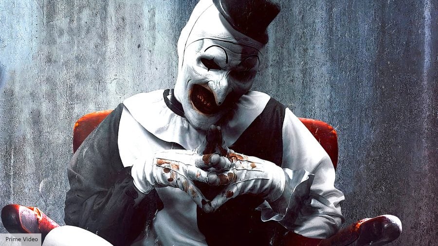 Terrifier: Art the Clown sitting menacingly on a red chair, covered in blood.
