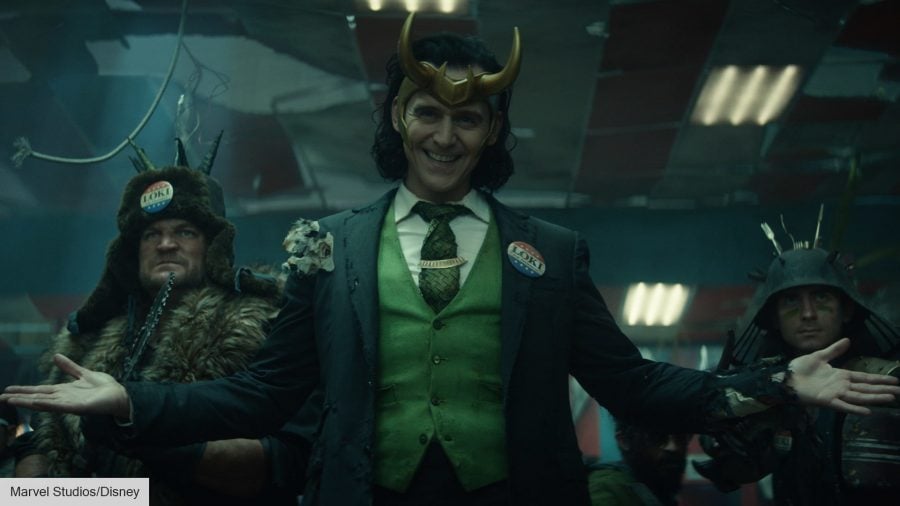 Loki, wearing their golden horns, and a three-piece suit, with two armed guards